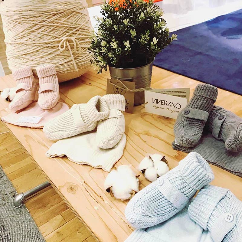 Collection of baby booties and hats on a wooden surface with yarn and a. plant