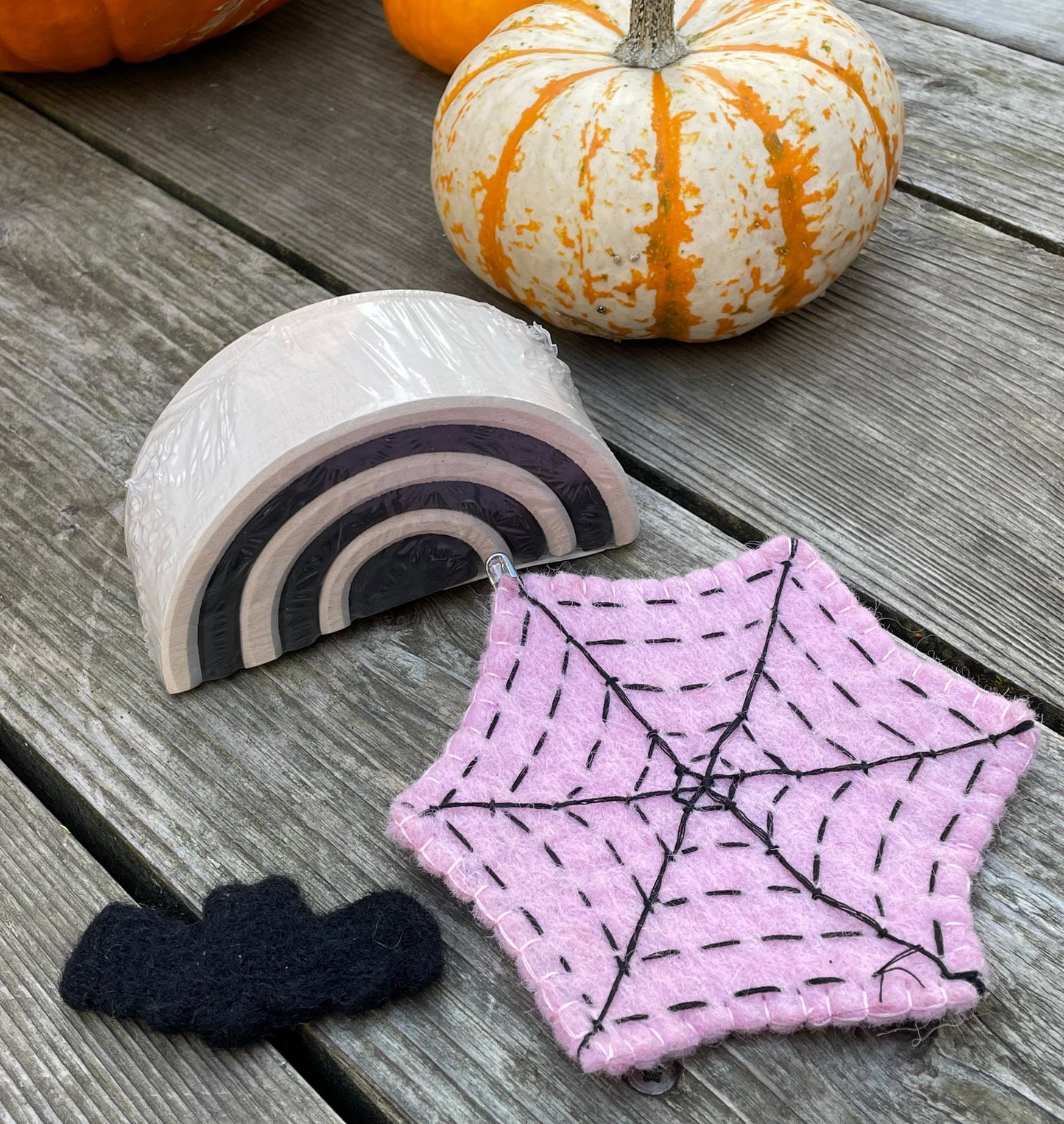 A black felt bat, a pink spider web, and a small monochrome arch with pumpkins