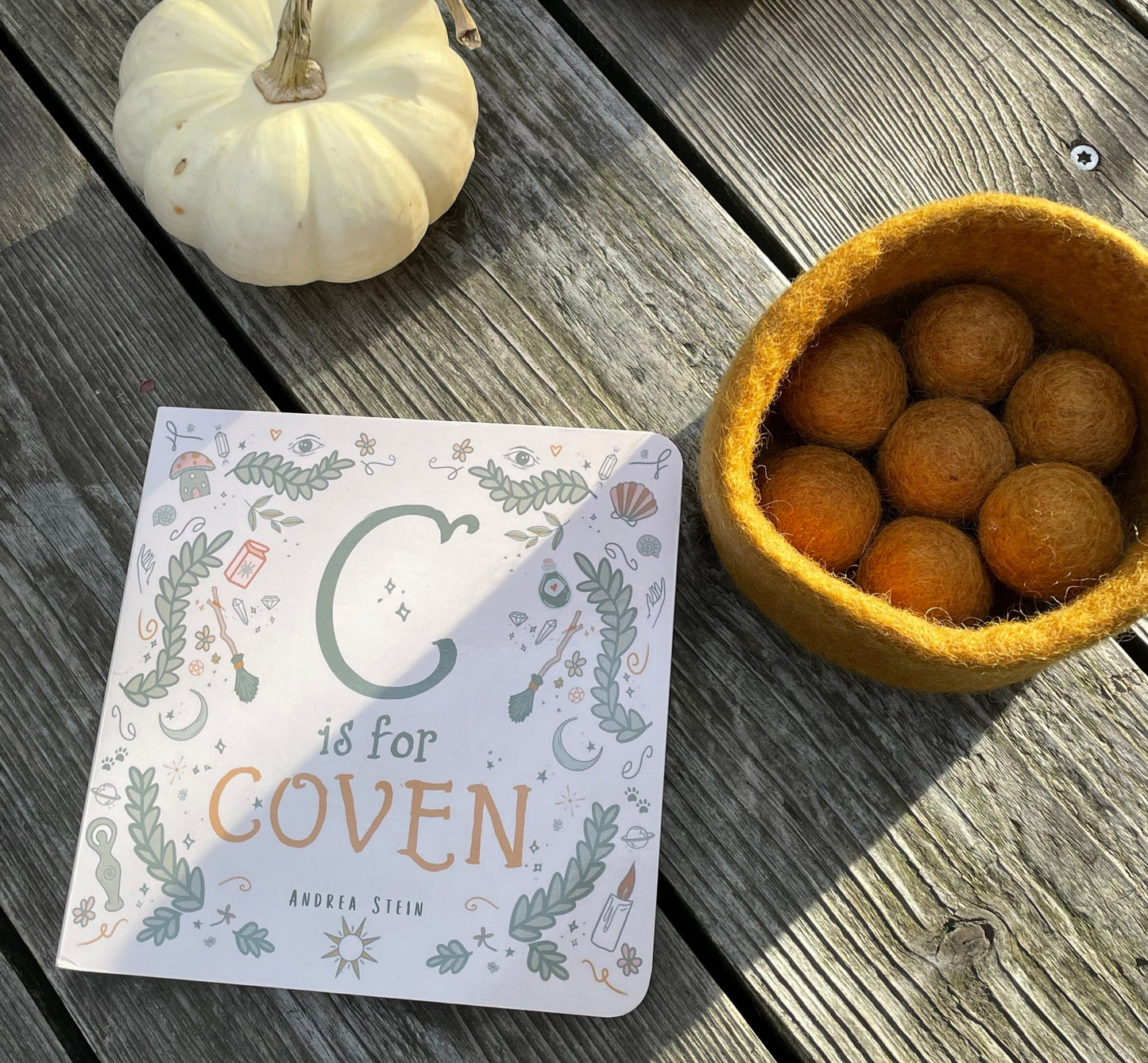 C is for coven board book and caramel felt balls & bowl in a booden table with pumpkins