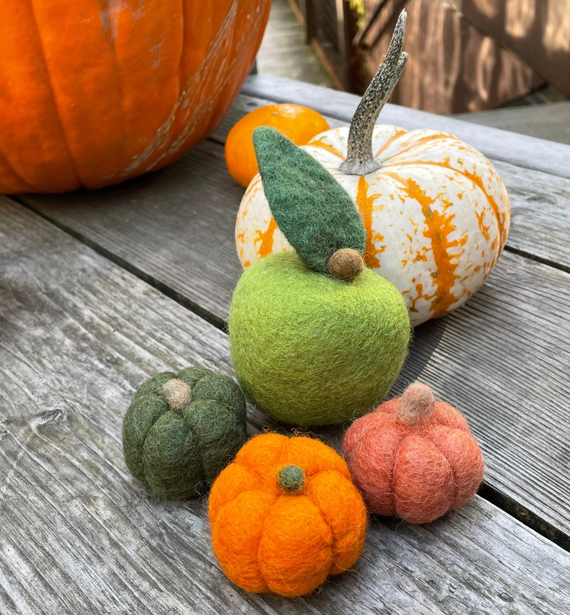 Felt apples and pumpkins on a wooden table with pumpkins in the background