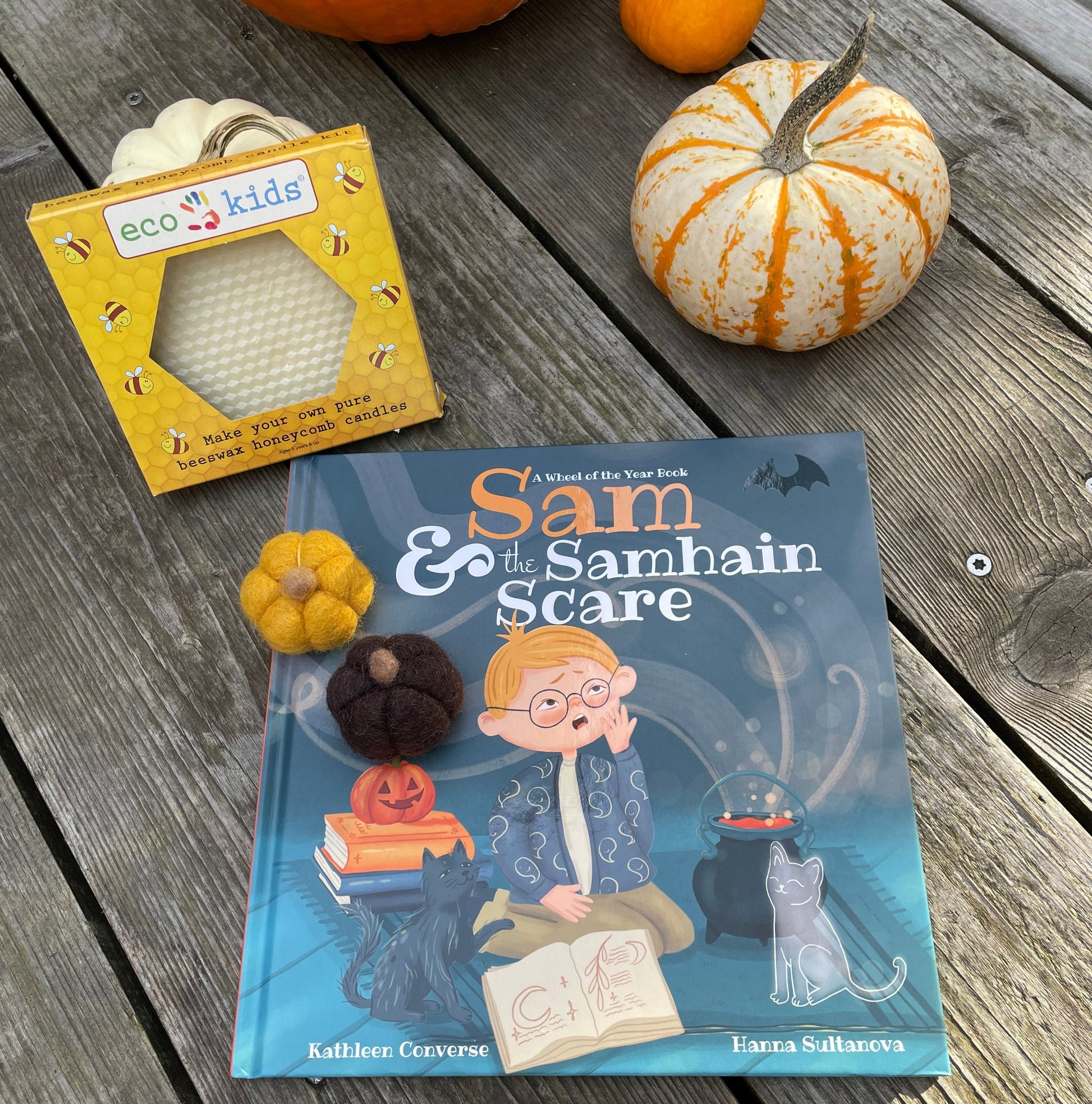 A Halloween book, candle making set, and felt pumpkins on a wooden table with pumpkins