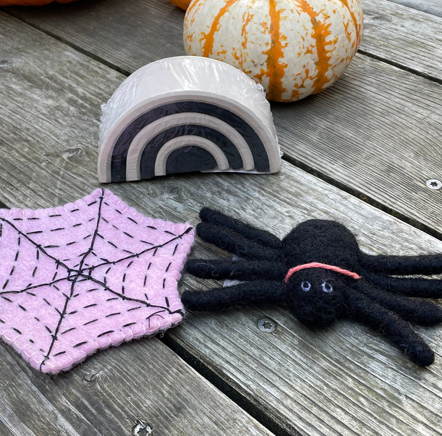 A pink spider web, a felt spider, and a small monochrome arch with pumpkins in the background