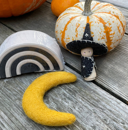 A witch peg doll, a gold felt moon, and a small monochrome arch with pumpkins in the background