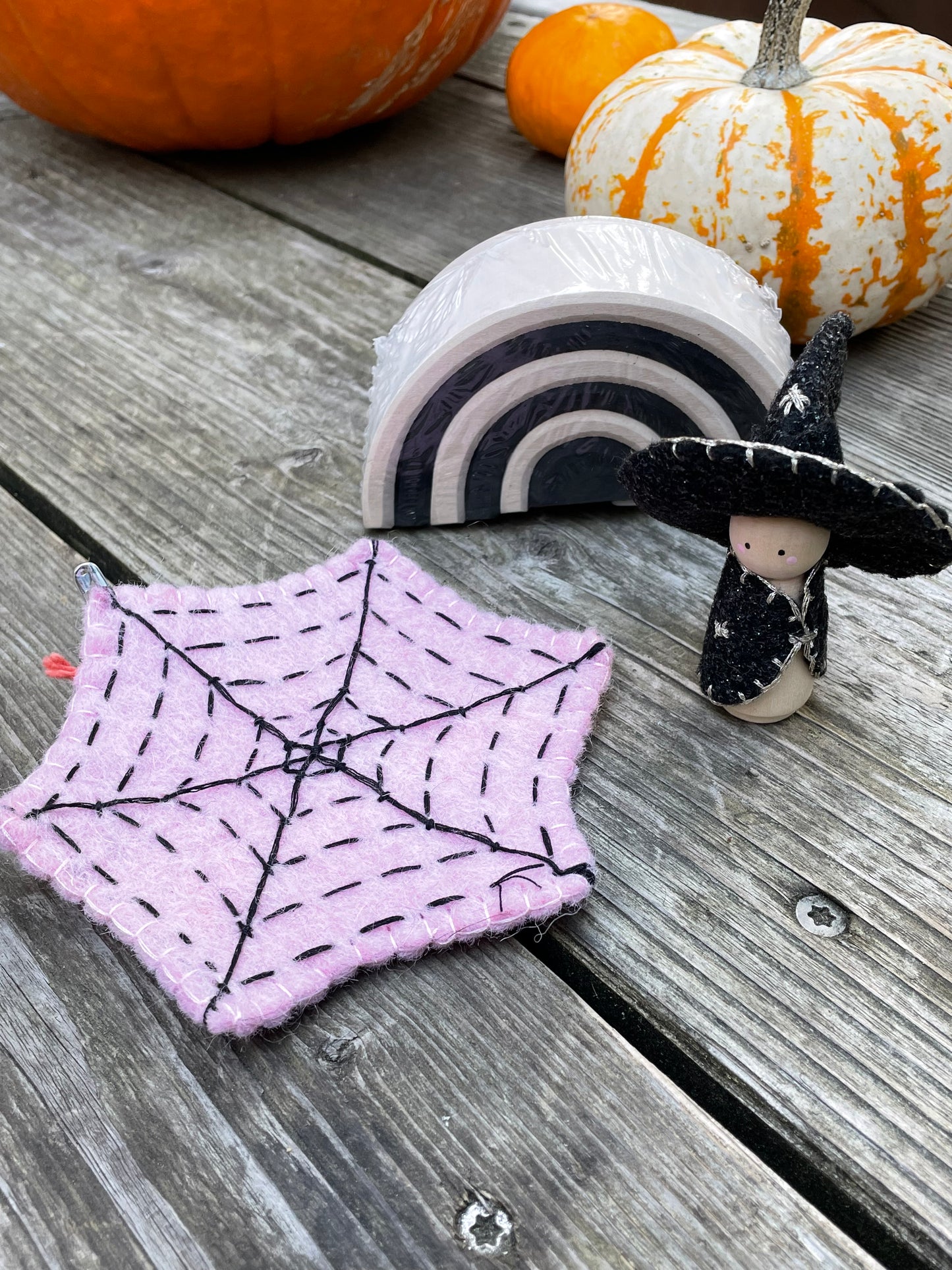 A pink felt spider web, a witch peg doll, and a small monochrome arch with pumpkins in the background