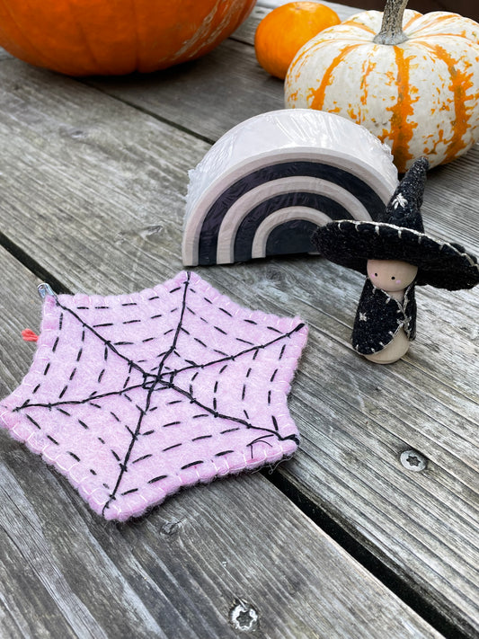 A pink felt spider web, a witch peg doll, and a small monochrome arch with pumpkins in the background