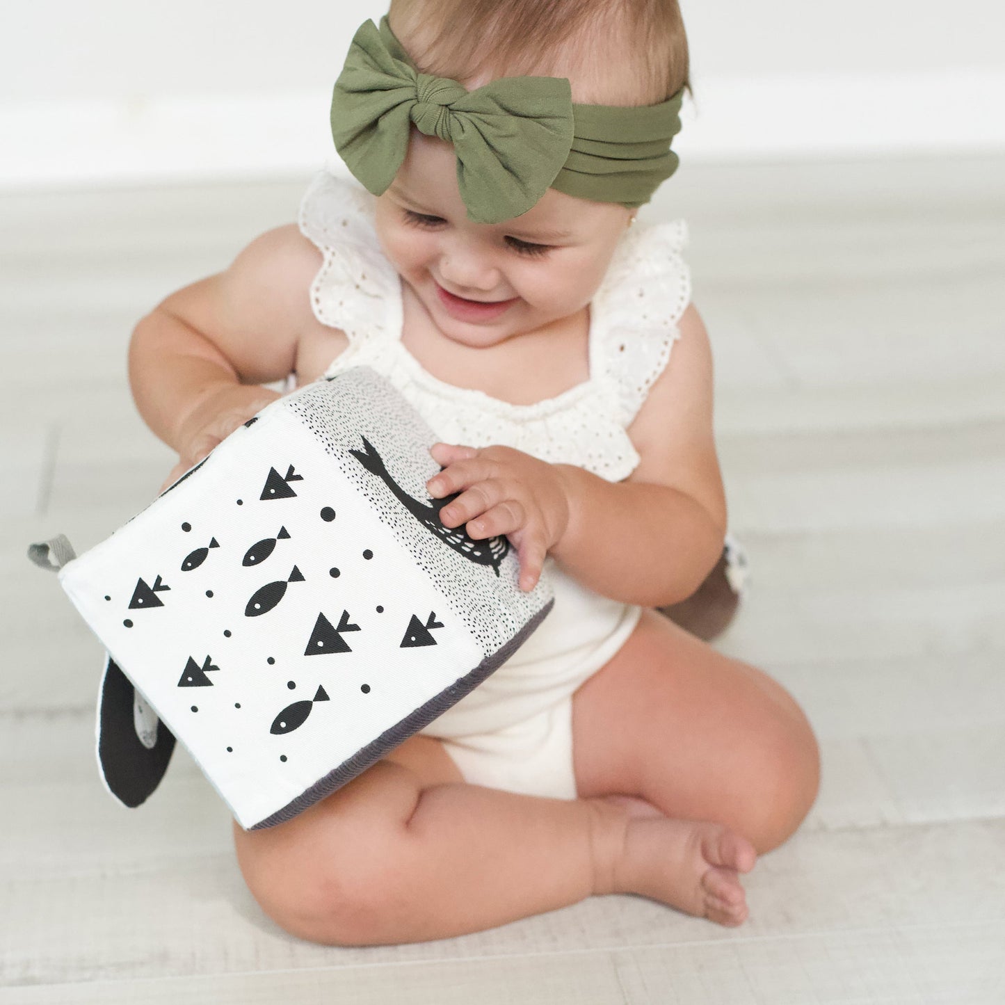 Baby holding a book with a green headband on a white background