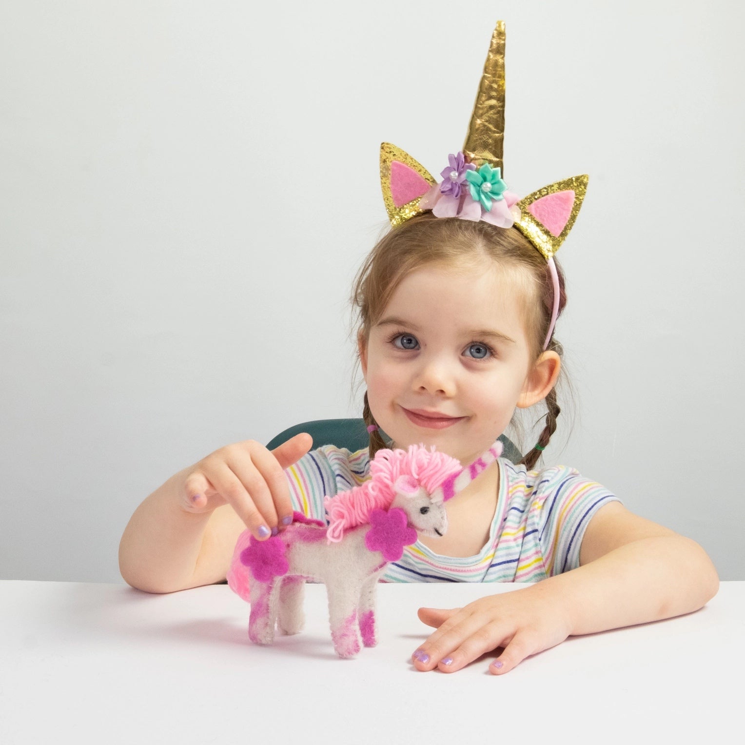 child wearing a unicorn headband playing with a pink felt unicorn