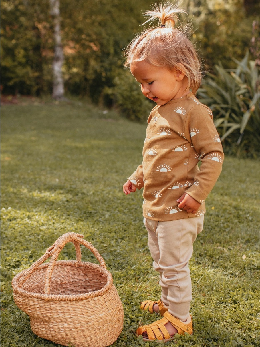 child standing outside by a straw basket wearing organic golden sun long sleeve tee