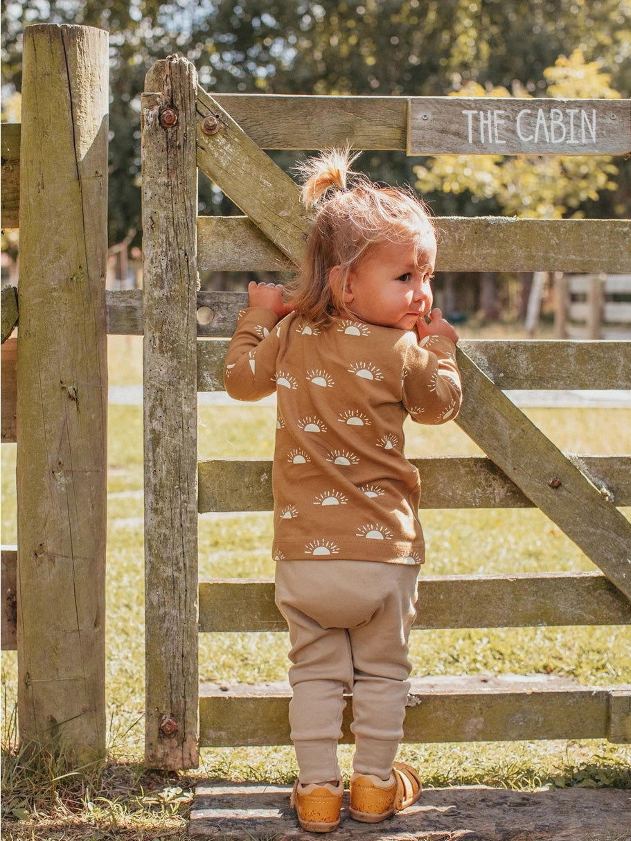child holding onto a fence wearing golden sun long sleeve tee