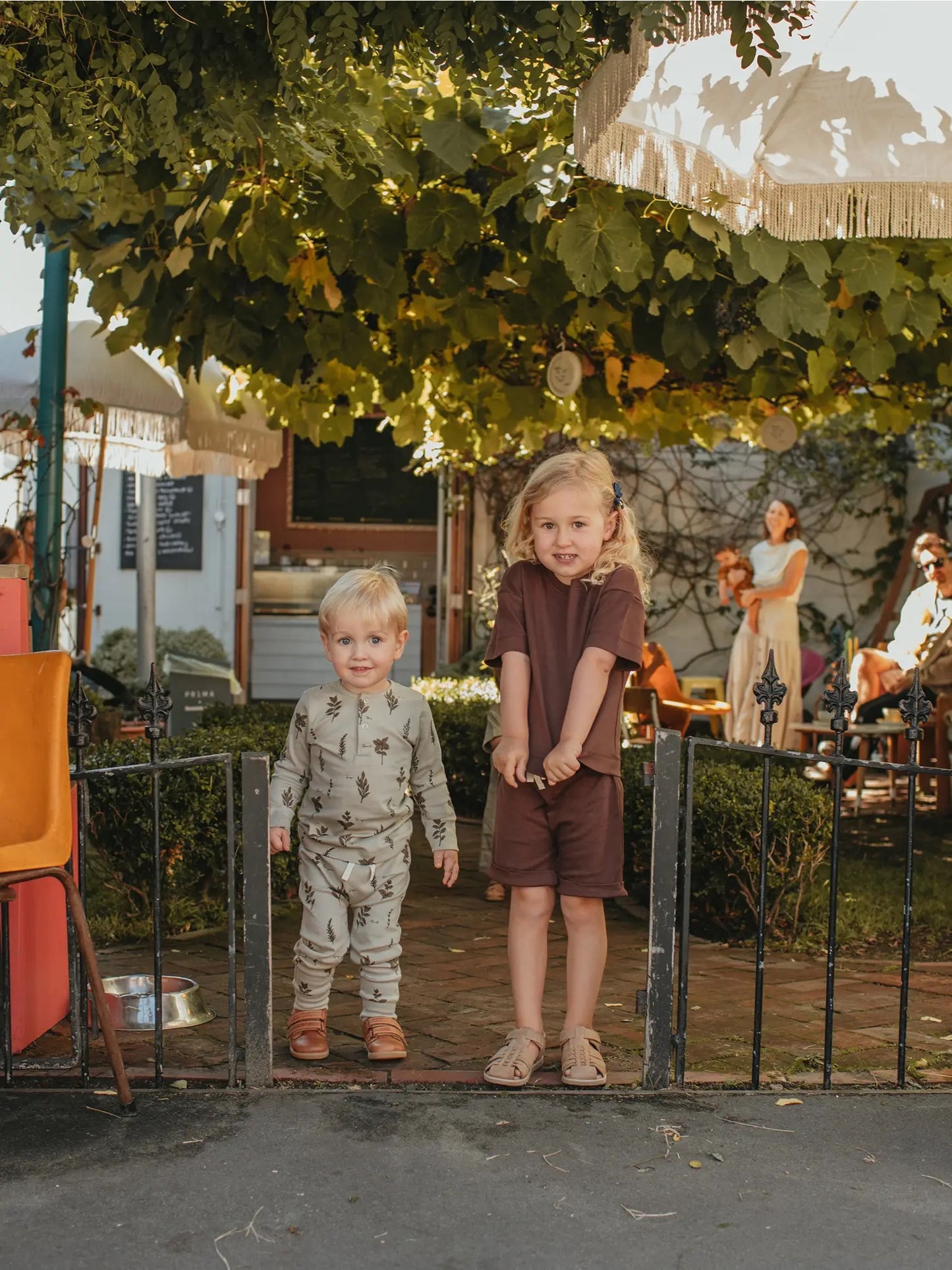 two children standing in front of a yard gate wearing Ziwi Baby sets