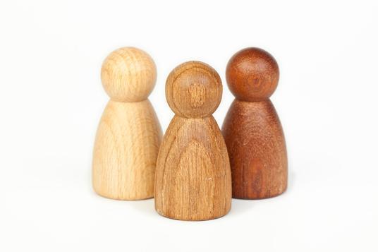 Three wooden peg people, unpainted, in different types of wood