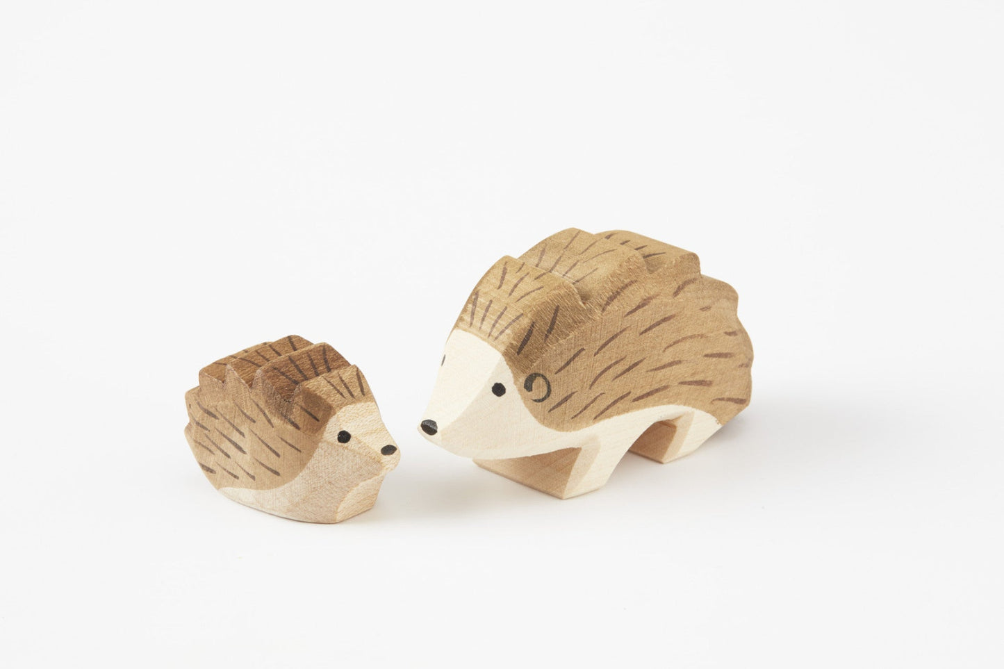 small and Large wooden hand carved Hedgehogs looking at each other on a white back ground