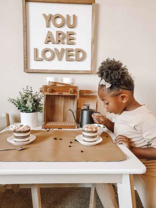 Child sitting at a table with a hot chocolate with a poppie barista on a shelf in the back ground