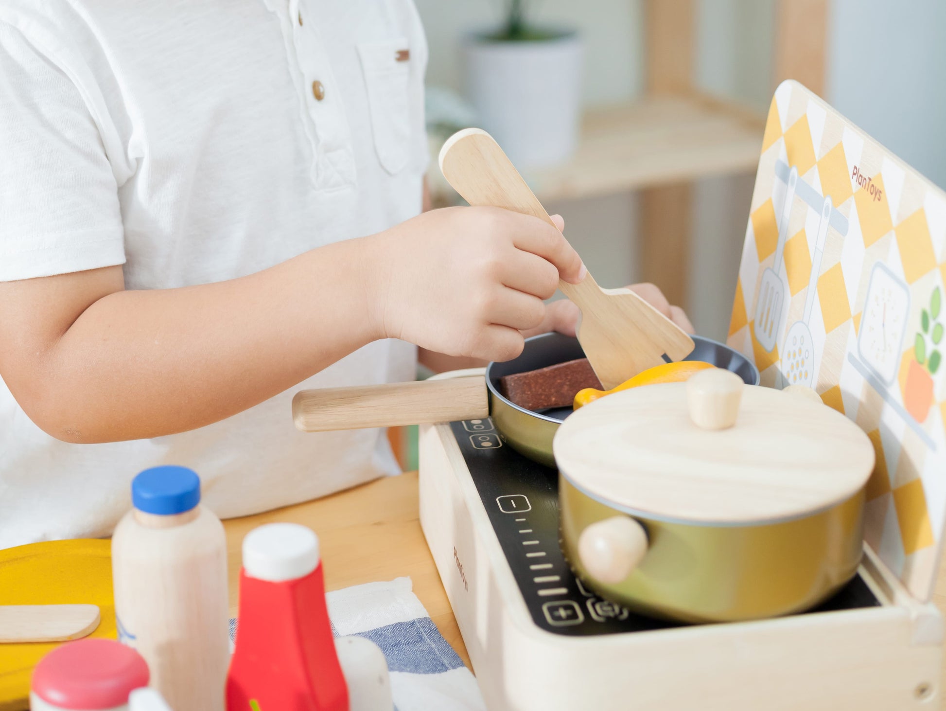 child playing in a play kitchen with Cooking Utensils Set by plan toys