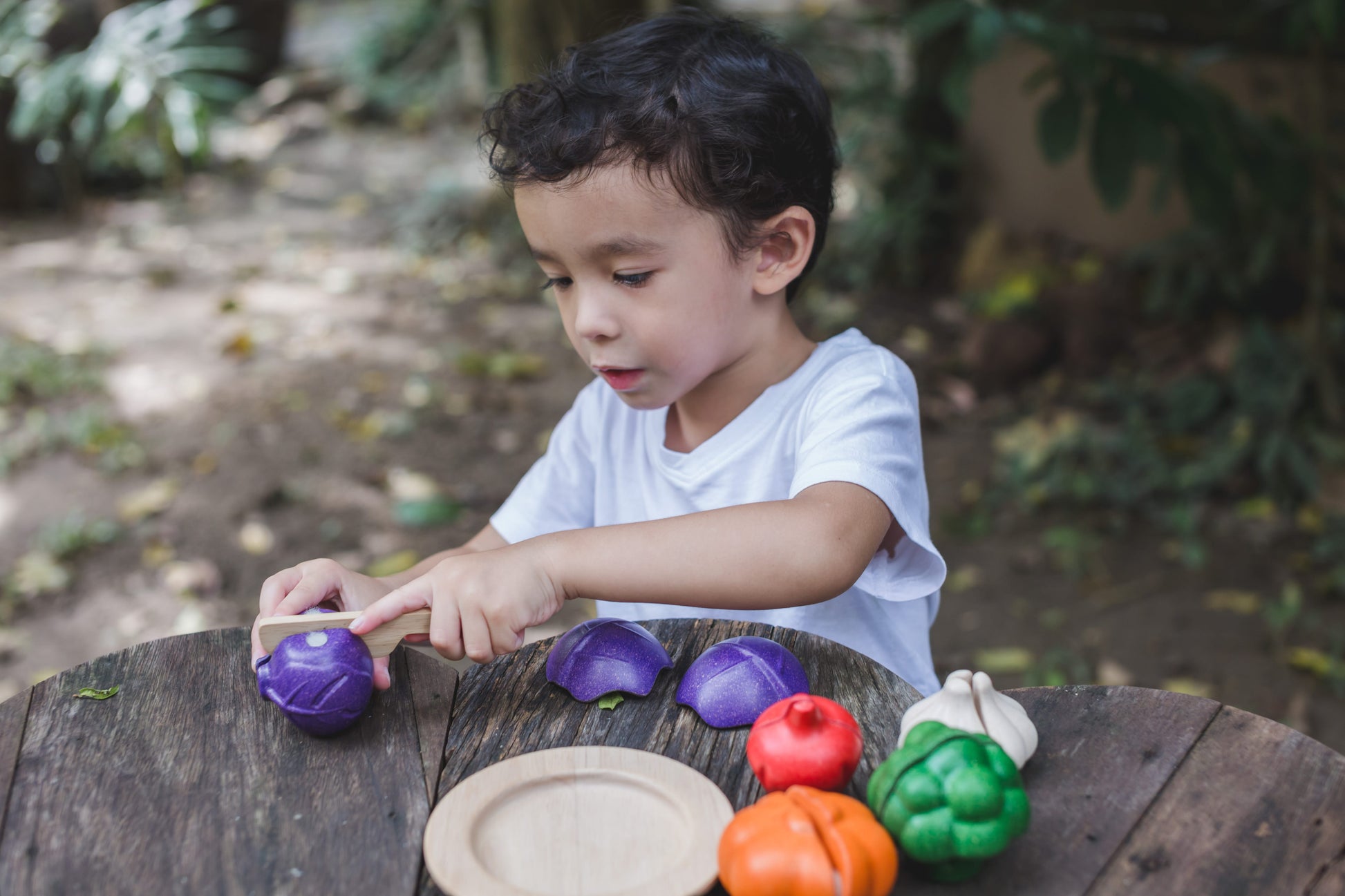 A child playing with a wooden vegetables on a wood table outdoors. The child scuttling the onion