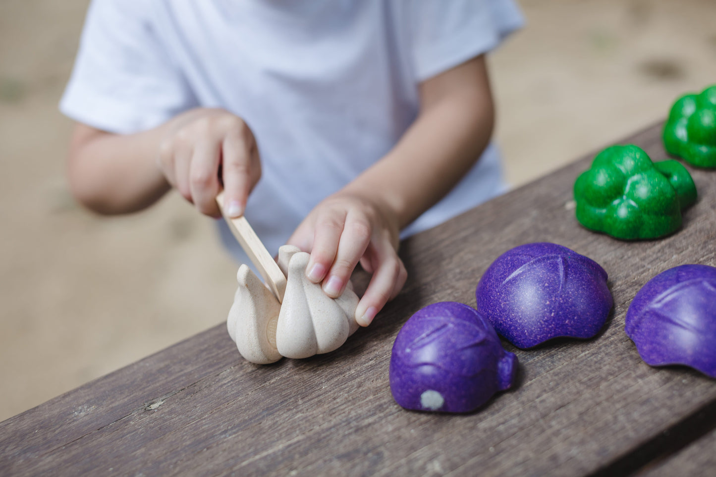 A child cutting a wooden garlic bulb on a wooden table