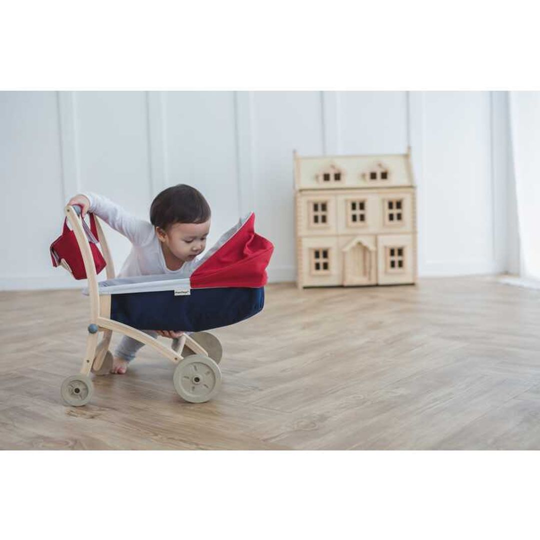 Toddler playing with a Doll Stroller by Plan Toys