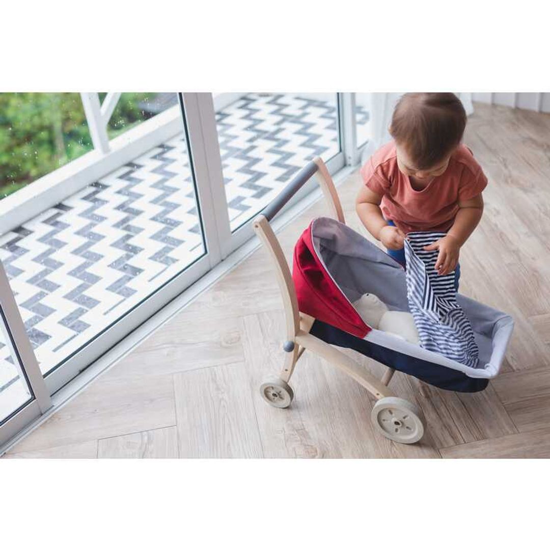 Toddler playing with a Doll Stroller by Plan Toys