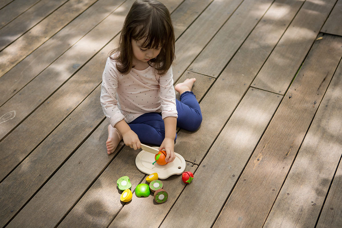 Child out side on a deck playing with the plan toys Assorted Fruit Set