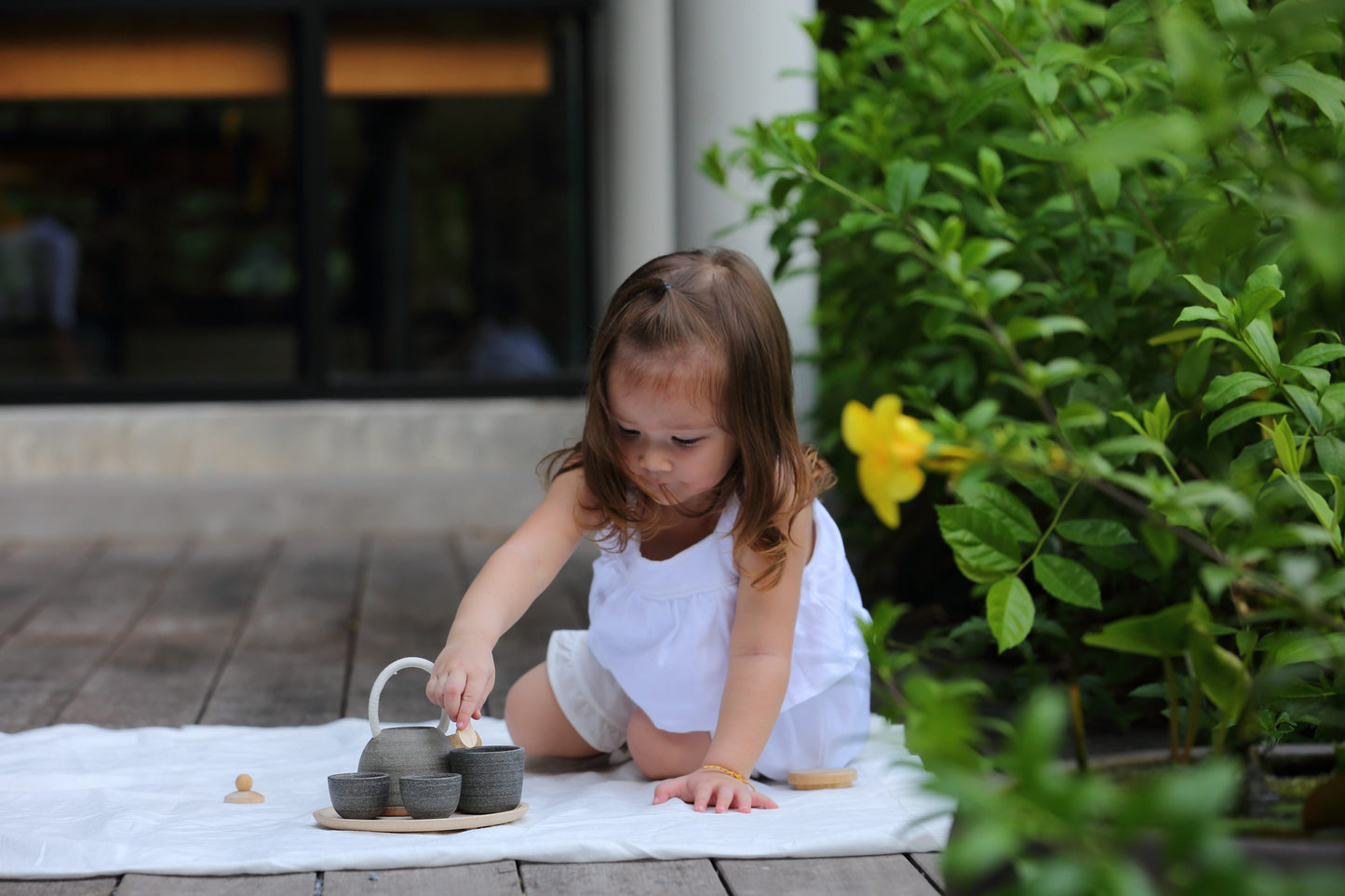 Child sitting outside playing with classic tea set by PlanToys