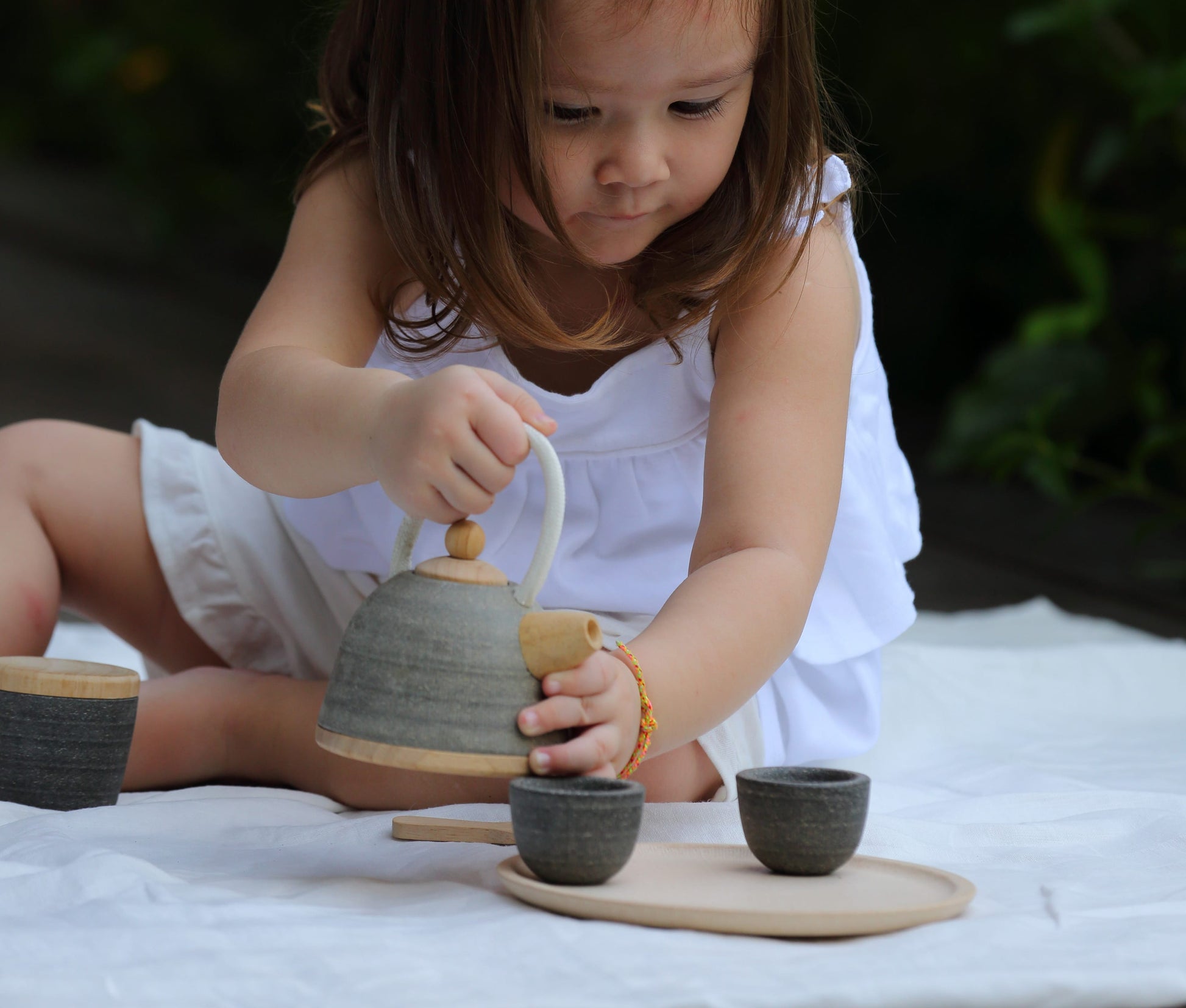 Child sitting outside playing with classic tea set by PlanToys