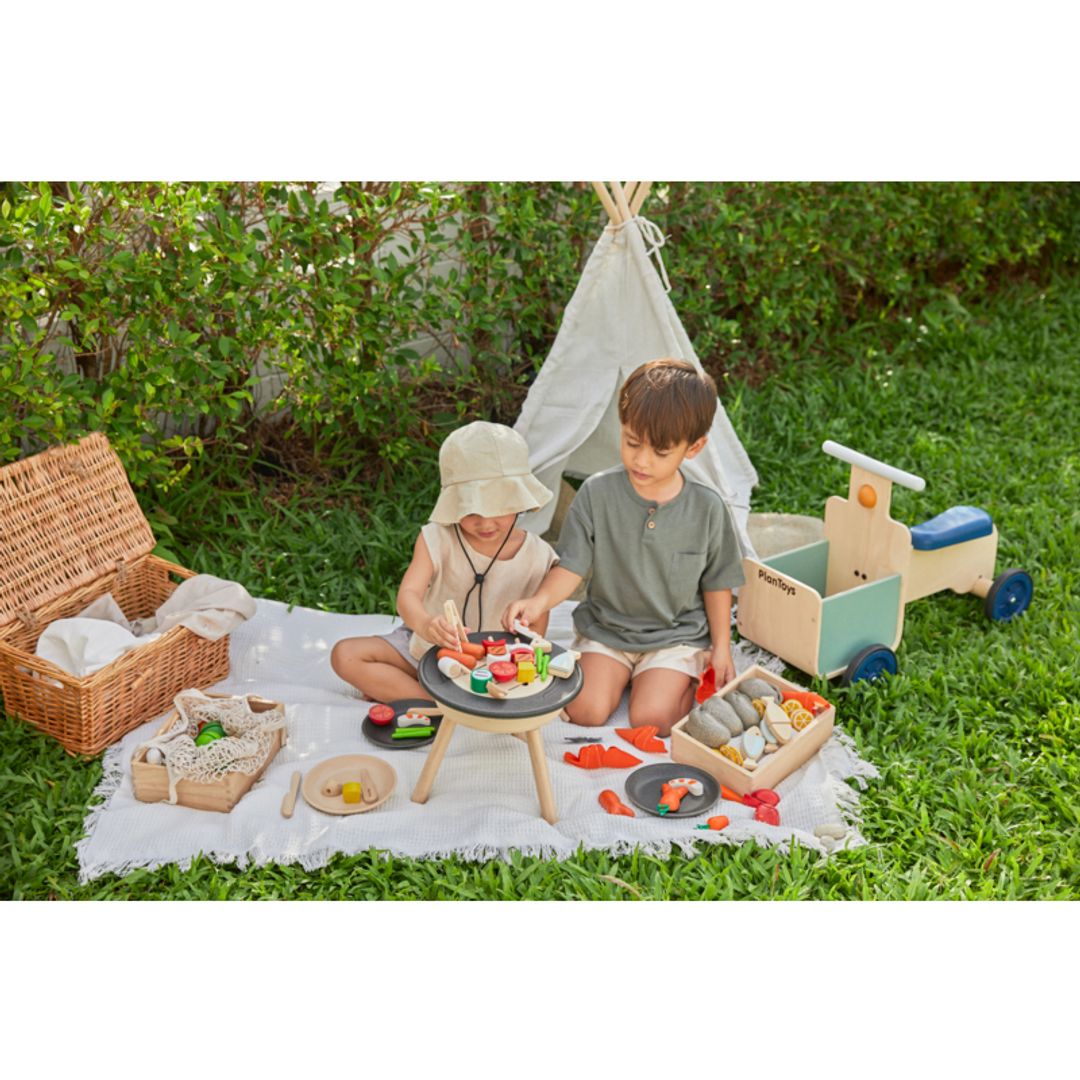 Kids playing outside BBQ Playset by Plan Toys on a blanket with a kids size tent