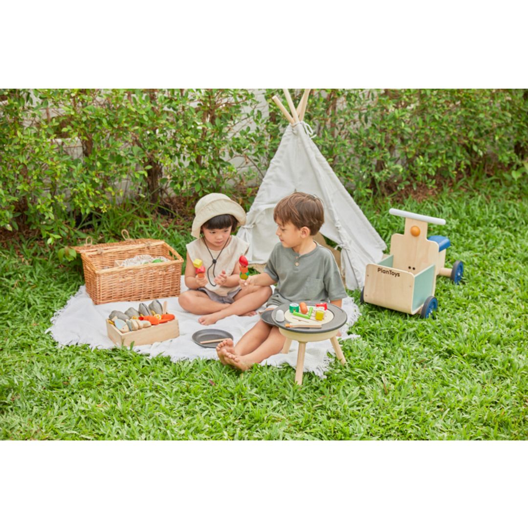 Kids playing outside BBQ Playset by Plan Toys on a blanket with a kids size tent