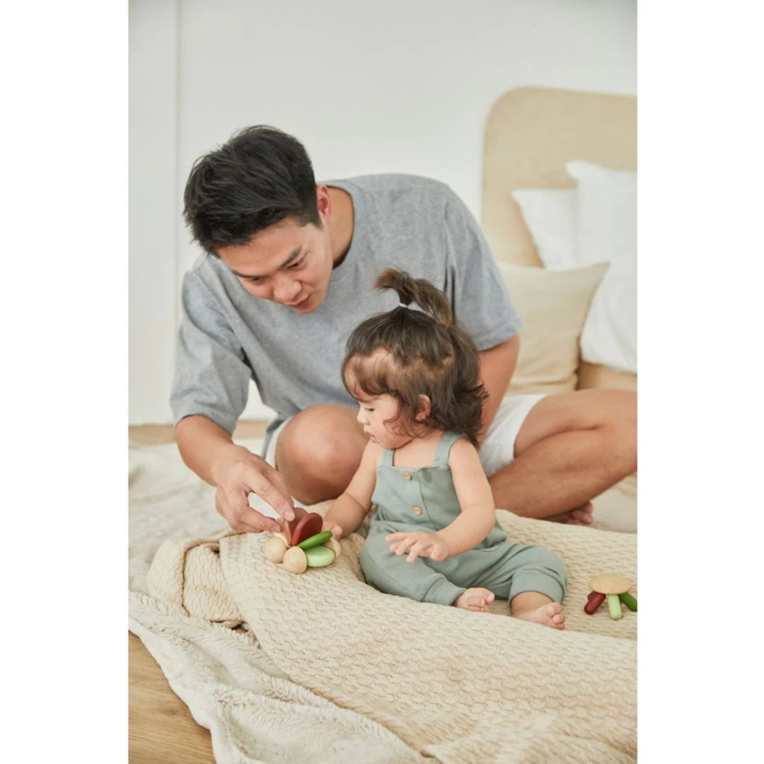 A child and parent playing with baby car by Plan Toys on a bed