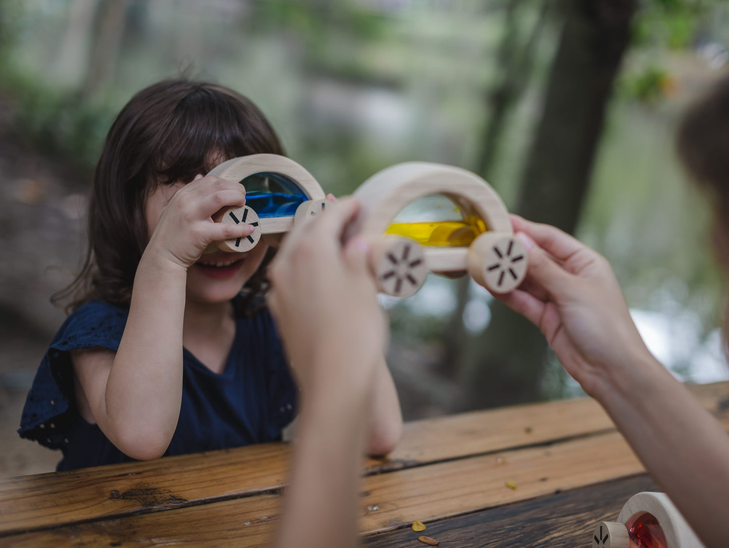 children sitting at a wooden table outdoors looking through wautomobiles