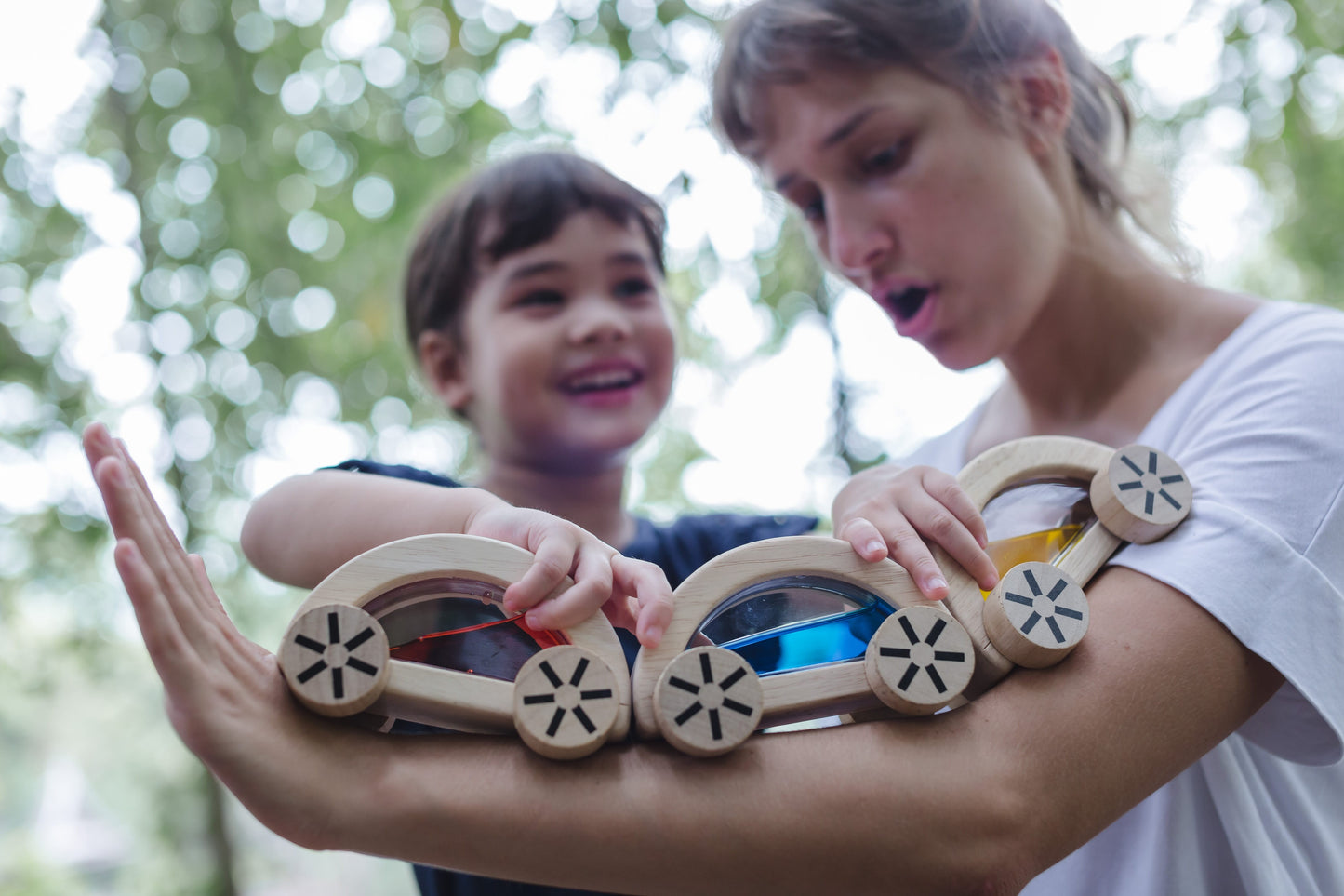 child playing with wautomobiles by running them on an adult's arm