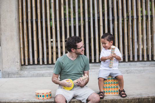Adult and a child sitting outside playing with toy instruments by PlanToys