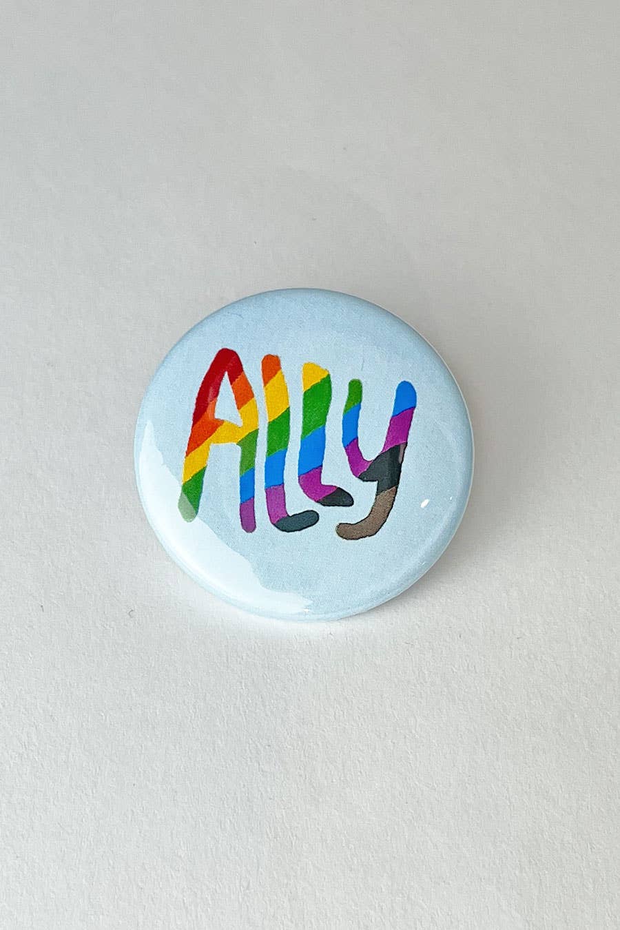 A white pinback button with the word "Ally" printed on it in pride flag colors