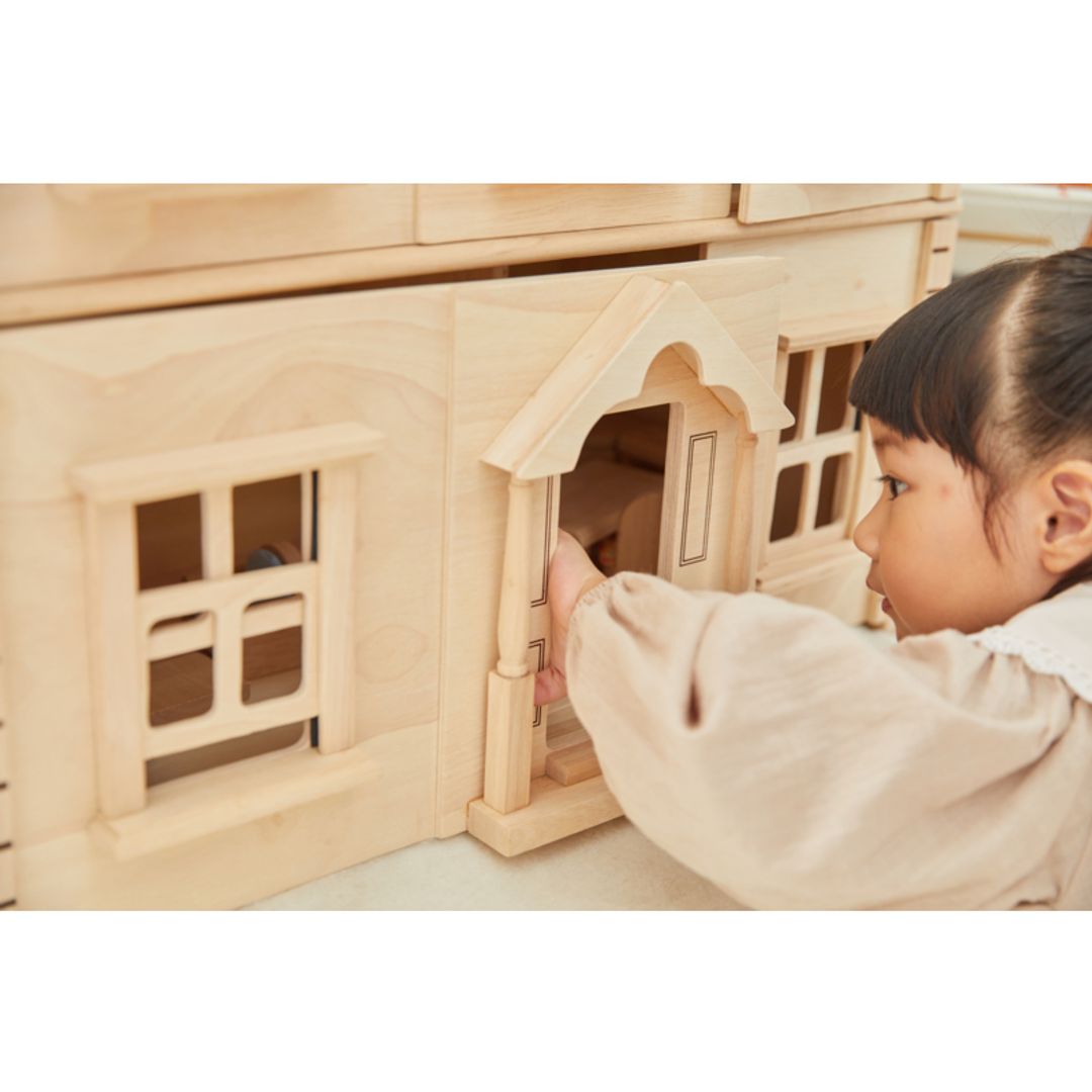 Child playing with a Victorian Dollhouse by Plan Toys