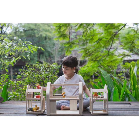 Child playing with Slide N Go Doll house with tree's behind them by Plan Toys