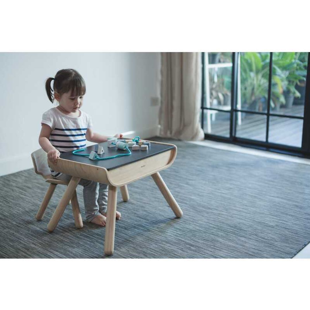 child sitting at the kids black Table & Chair Set By Plan Toys