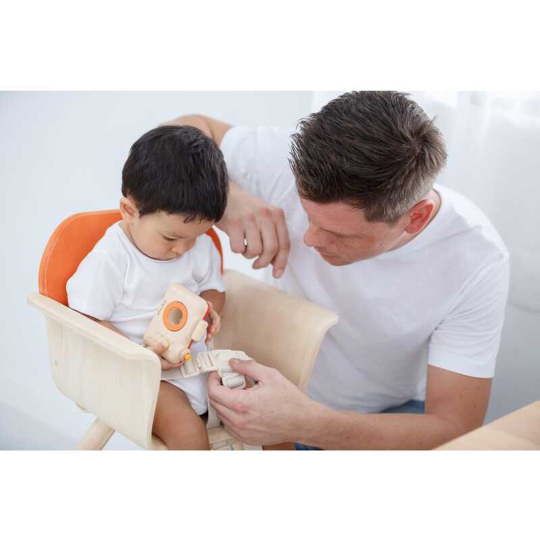 parent unbuckling the plan toys High Chair - Orange