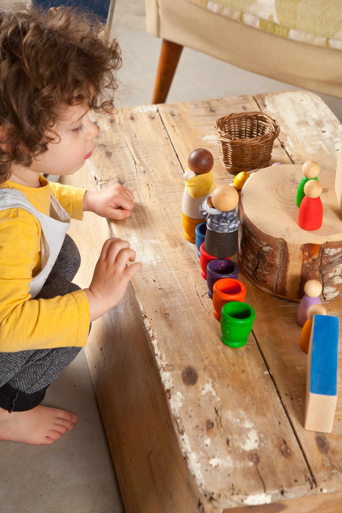 A child playing with colorful wooden peg people and rainbow wooden cups on a wood table.