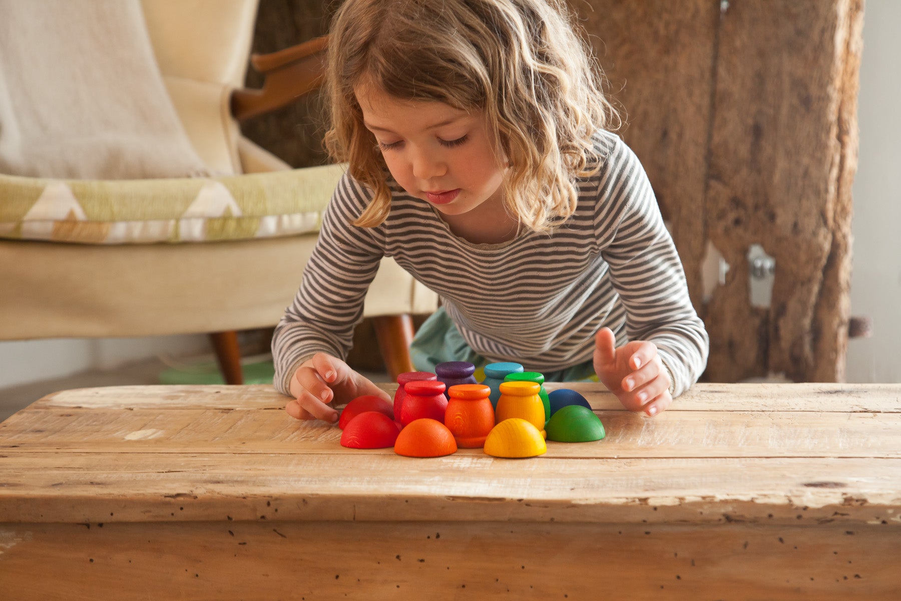 A child playing with rainbow wooden cups and bowls on a wooden table.