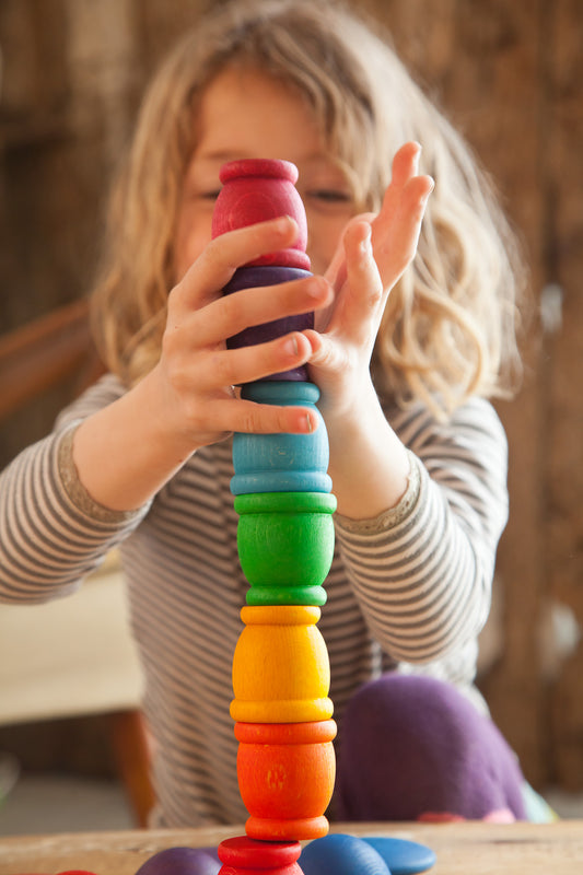 A child stacking rainbow wooden cups.