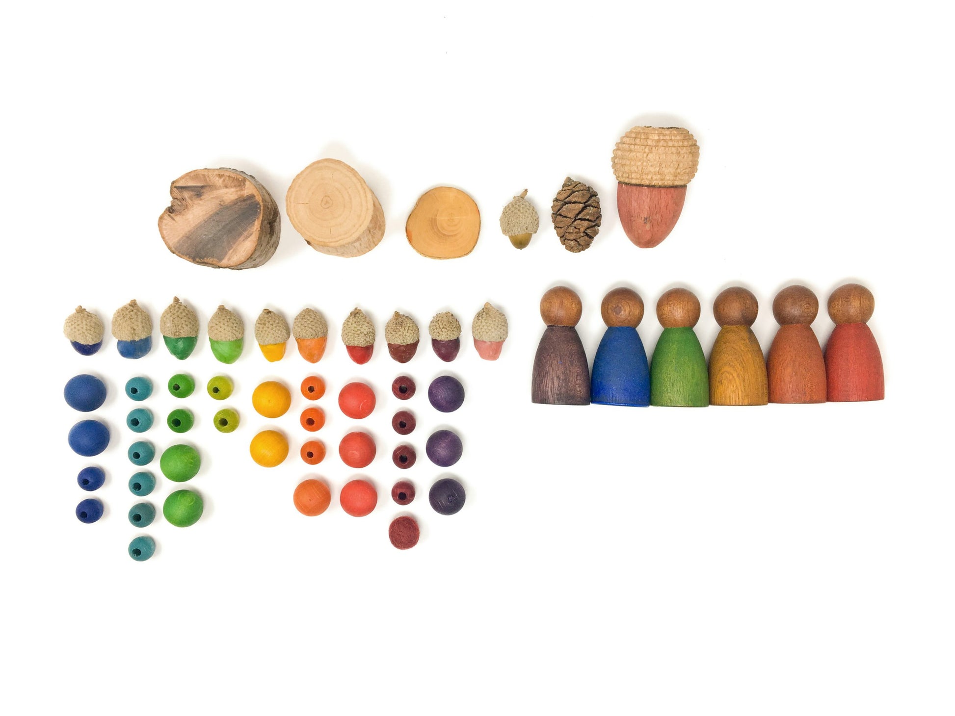 A series of small elements arranged on a plain surface. On top, three round pieces of wood, a small acorn, a pinecone, and a large acorn are arranged in a row. Below and to the left, small acorns and beads of various sizes are arranged in columns based on their color. To the right, six wooden peg people are arranged in a row based on their color, from left to right in the reverse order of the colors of the rainbow