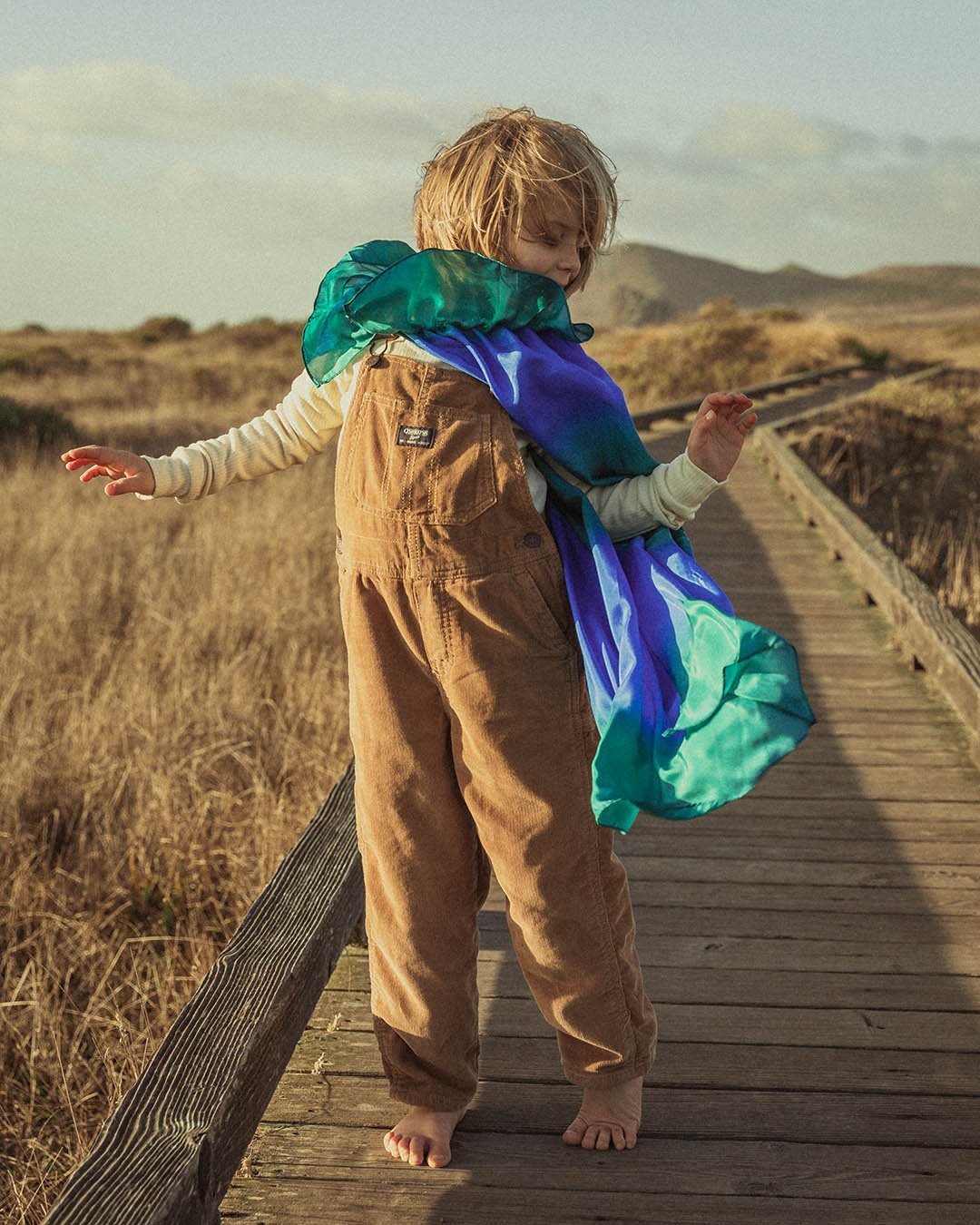 ocean silk cape on a child on a board walk in overalls
