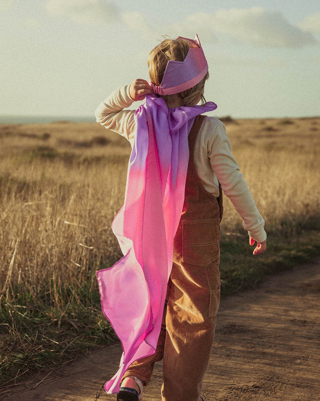 Child walking in a field wearing Blossom Reversible Silk Play Cape and blossom crown