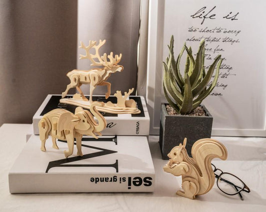 Three assembled 3D wooden puzzles on a desk, from left to right of a moose, elephant, and squirrel