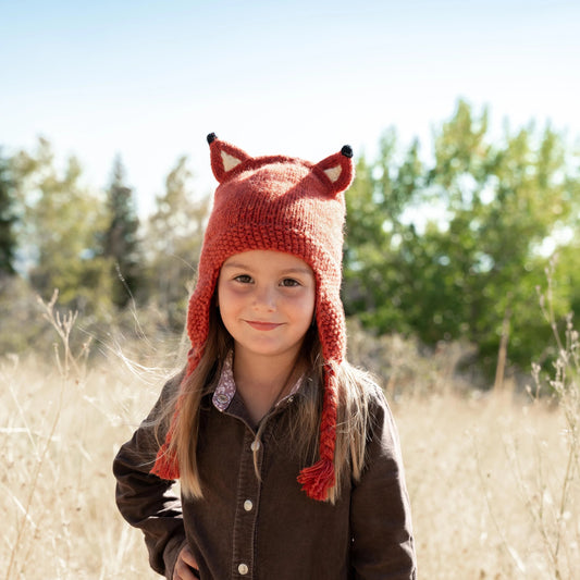 Child standing in a field wearing wool fox animal hat