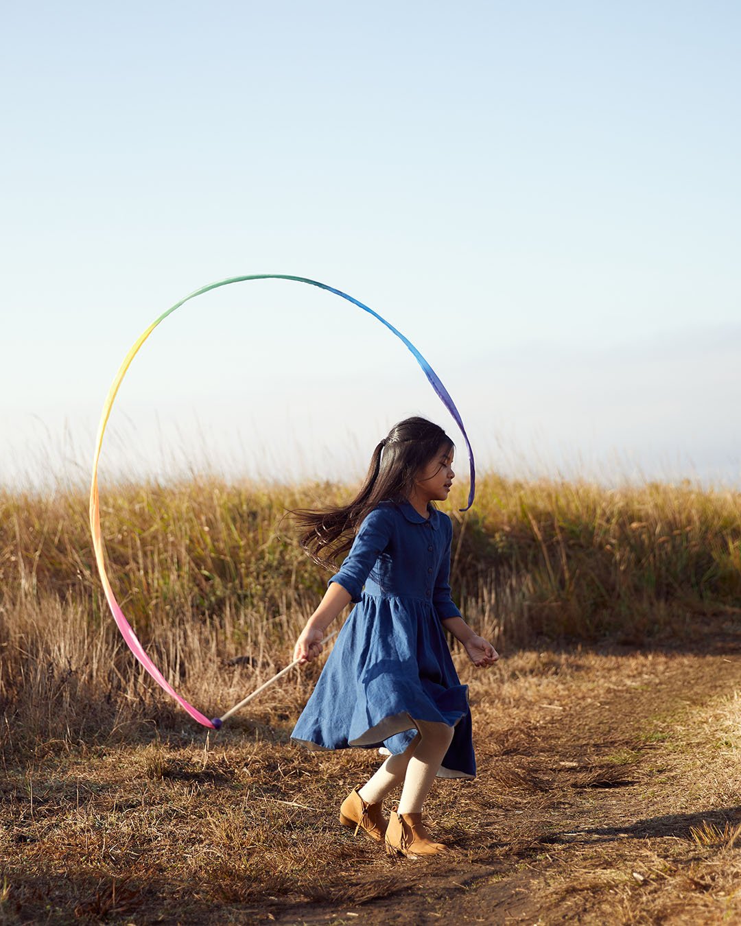 Child playing with Silk rainbow streamer in a field