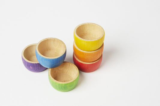 A set of six rainbow wooden bowls. From top to bottom, the yellow, orange, and red are stacked on top of each other. To the left, the purple and green are set next to each other with the purple on top