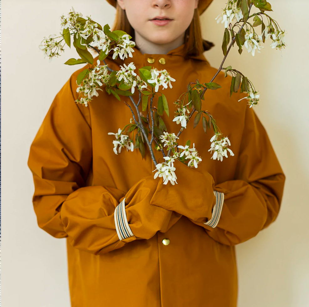 A child. holding branches with flowers wearing oak rain coat and rain mitts by FaireChild