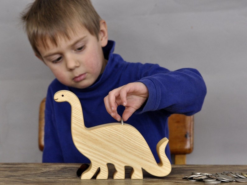 Child inserting coins in a wooden brontosaurus coin bank