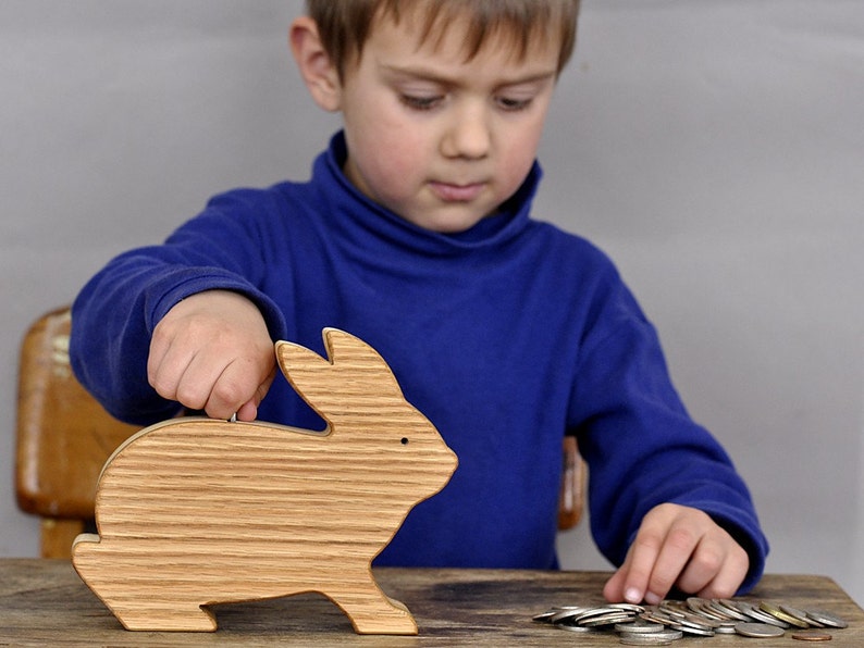 Child inserting coins in a wooden rabbit coin bank