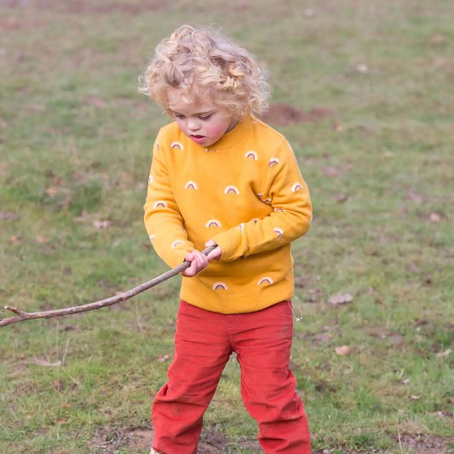 Child wearing "From One To Another" Rainbows Sweater and holding a stick